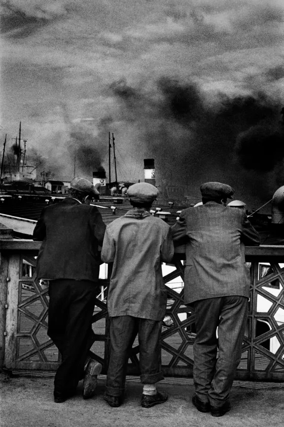 Three men leaning on a railing, looking out to sea.